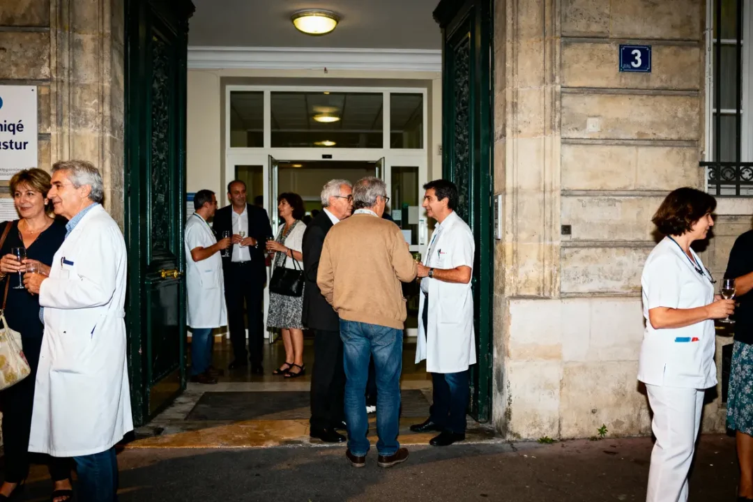 Personnes en discussion devant une entrée de clinique, médecins en blouses blanches, ambiance décontractée.