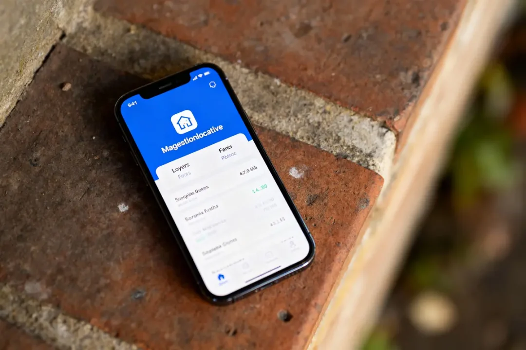 Smartphone affichant l'application "Magestionlocative" sur un écran, posé sur une surface en briques.