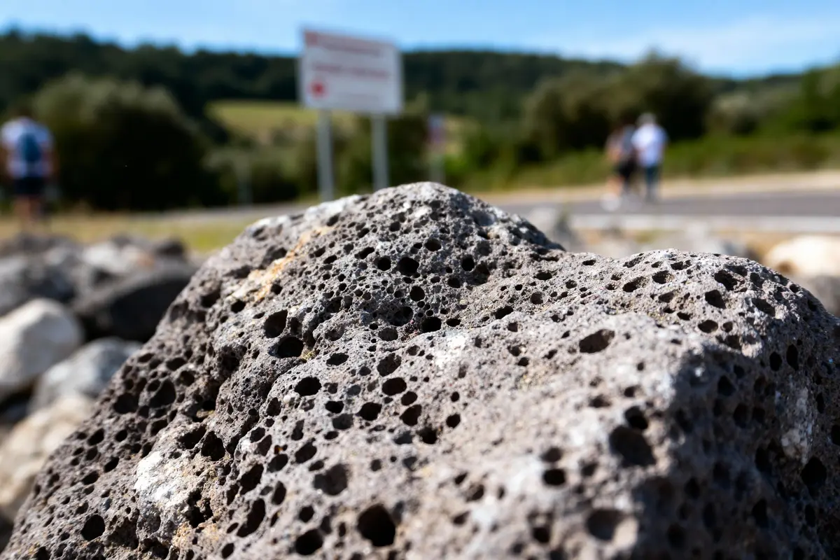 Gros plan sur une roche volcanique poreuse avec paysage flou en arrière-plan. Deux personnes floues à distance.