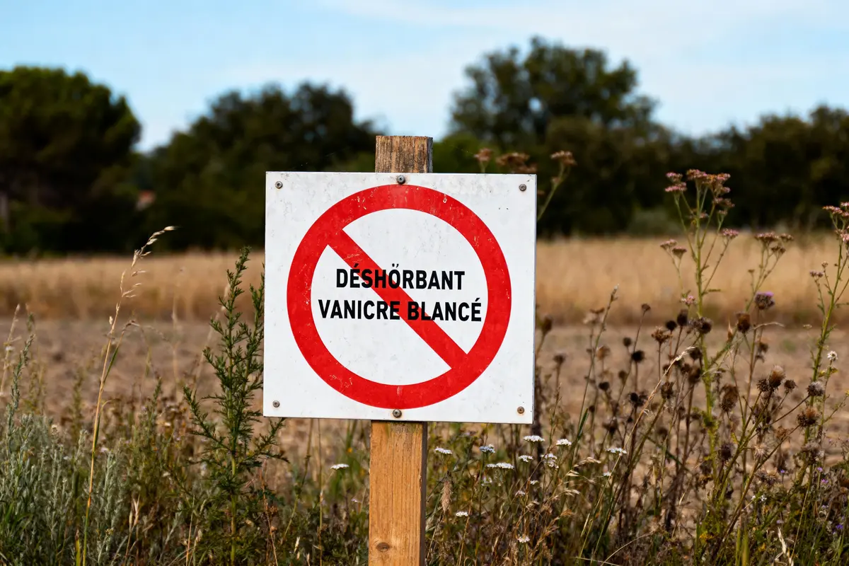 Panneau interdit, texte "Désherbant Vanicre Blancé", nature en arrière-plan, champ, végétation sauvage.