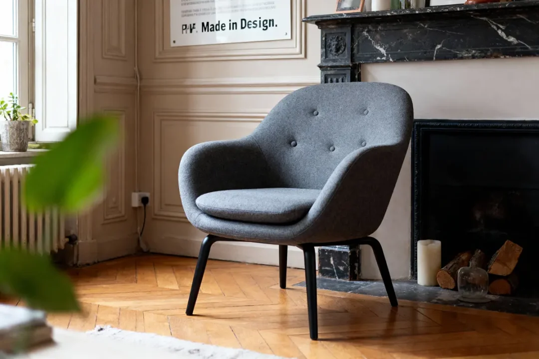 Fauteuil en tissu dans un intérieur minimaliste avec plante et affiche design, mur texturé en arrière-plan.