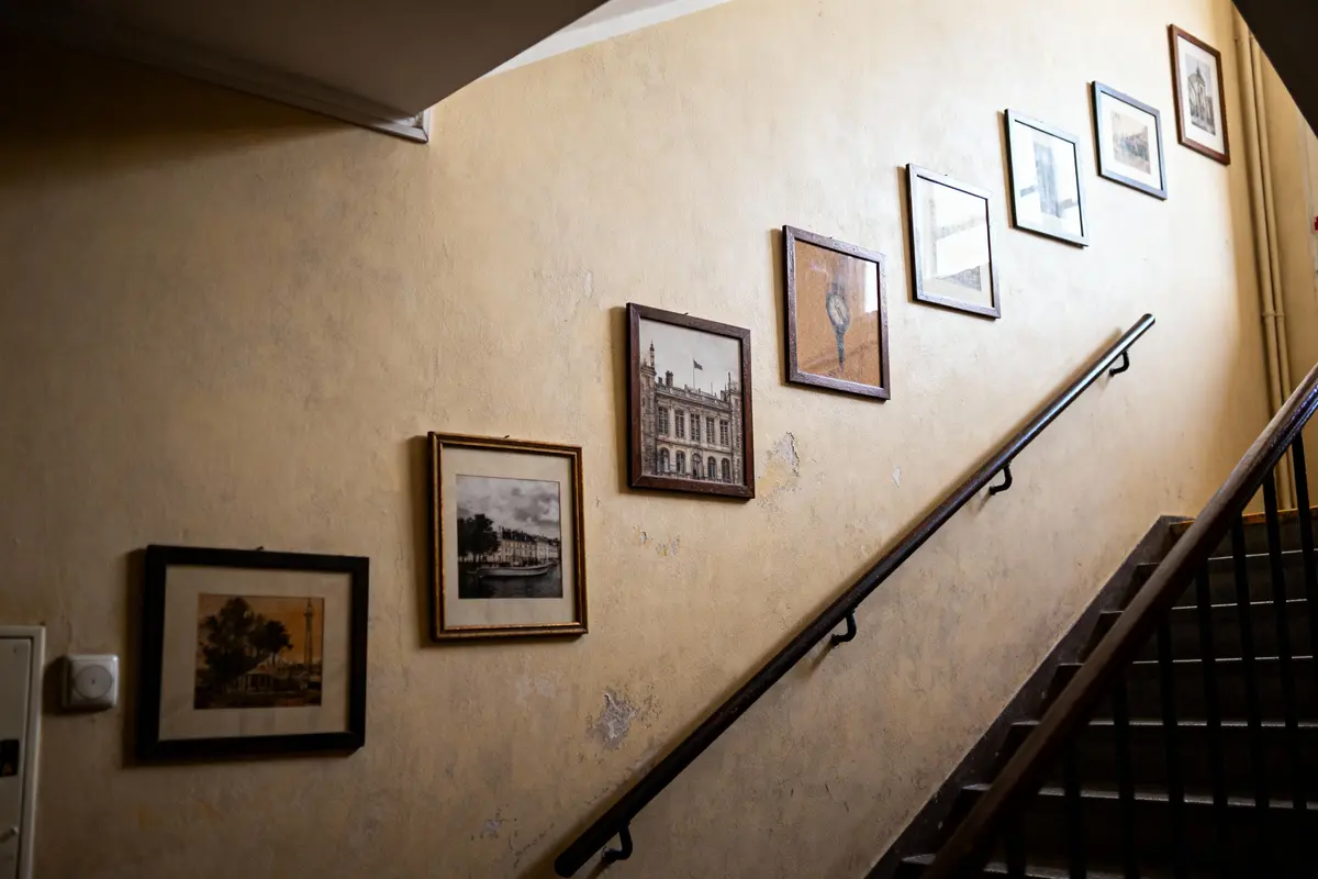 Tableaux encadrés accrochés sur un mur le long d'un escalier intérieur, lumière tamisée.