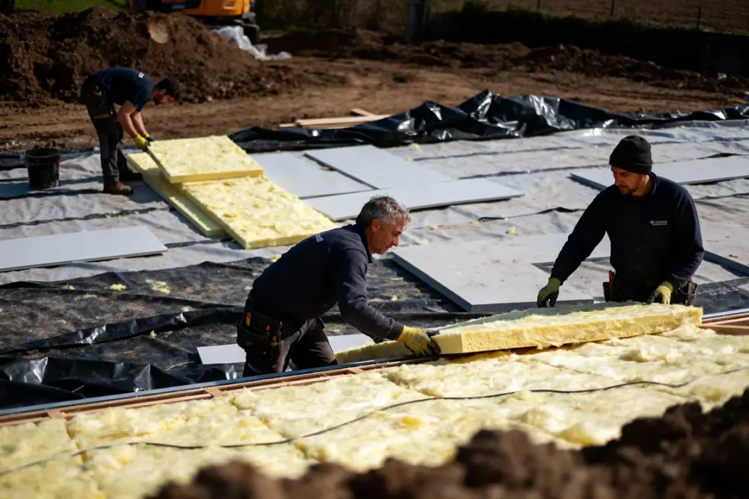 Des ouvriers posent des panneaux d'isolation sur un chantier de construction, utilisant des matériaux jaunes.