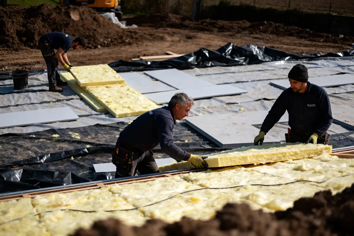 Des ouvriers posent des panneaux d'isolation sur un chantier de construction, utilisant des matériaux jaunes.