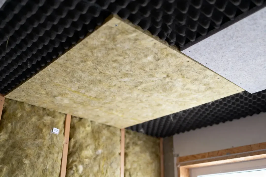 Isolation acoustique et thermique en laine minérale et mousse dans une pièce avec fenêtre visible.