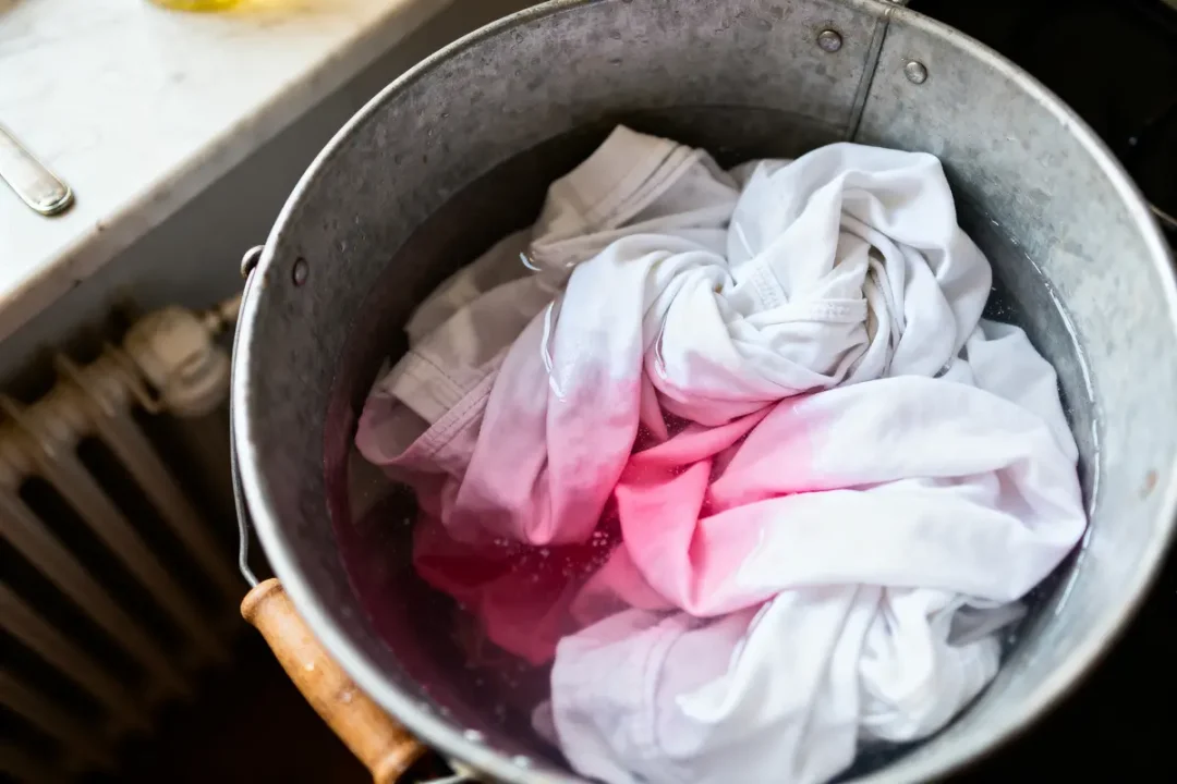 T-shirts blancs trempés dans un seau d'eau légèrement colorée en rose.