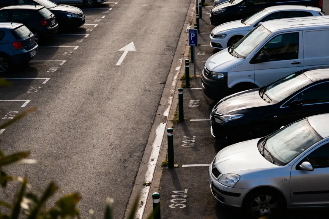 Parking extérieur, voitures alignées, places numérotées, flèche directionnelle au sol, matin ensoleillé.