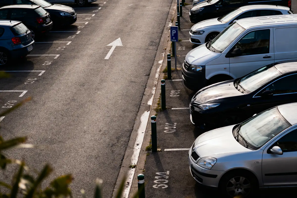 Parking extérieur, voitures alignées, places numérotées, flèche directionnelle au sol, matin ensoleillé.