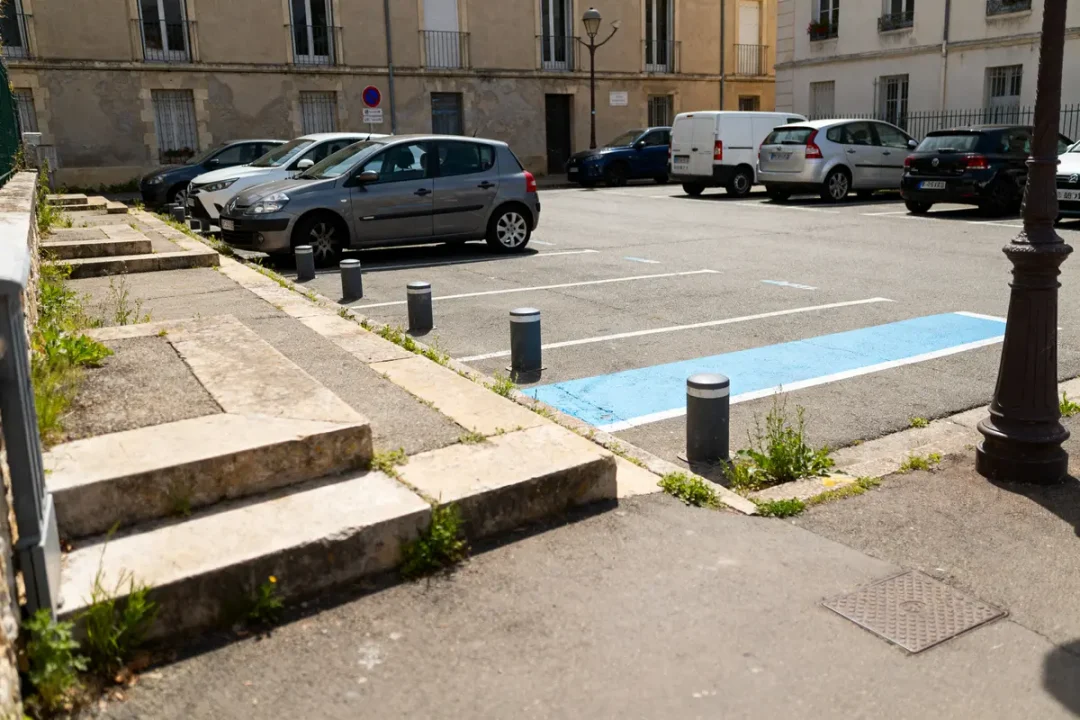 Place de parking avec voiture grise, zone bleue et obstacles en béton