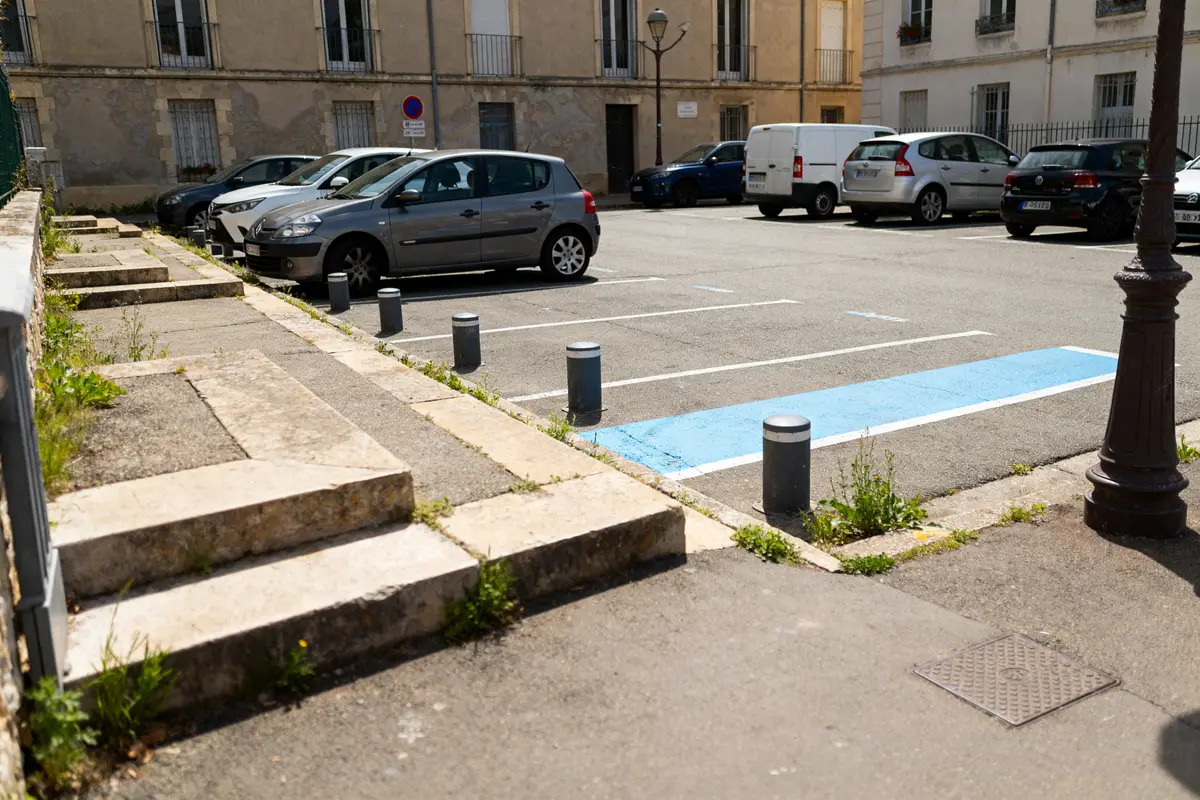 Place de parking avec voiture grise, zone bleue et obstacles en béton