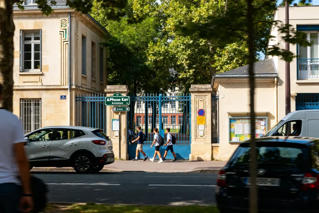 Des piétons traversent devant le portail bleu du lycée sur rue Alphonse Karr