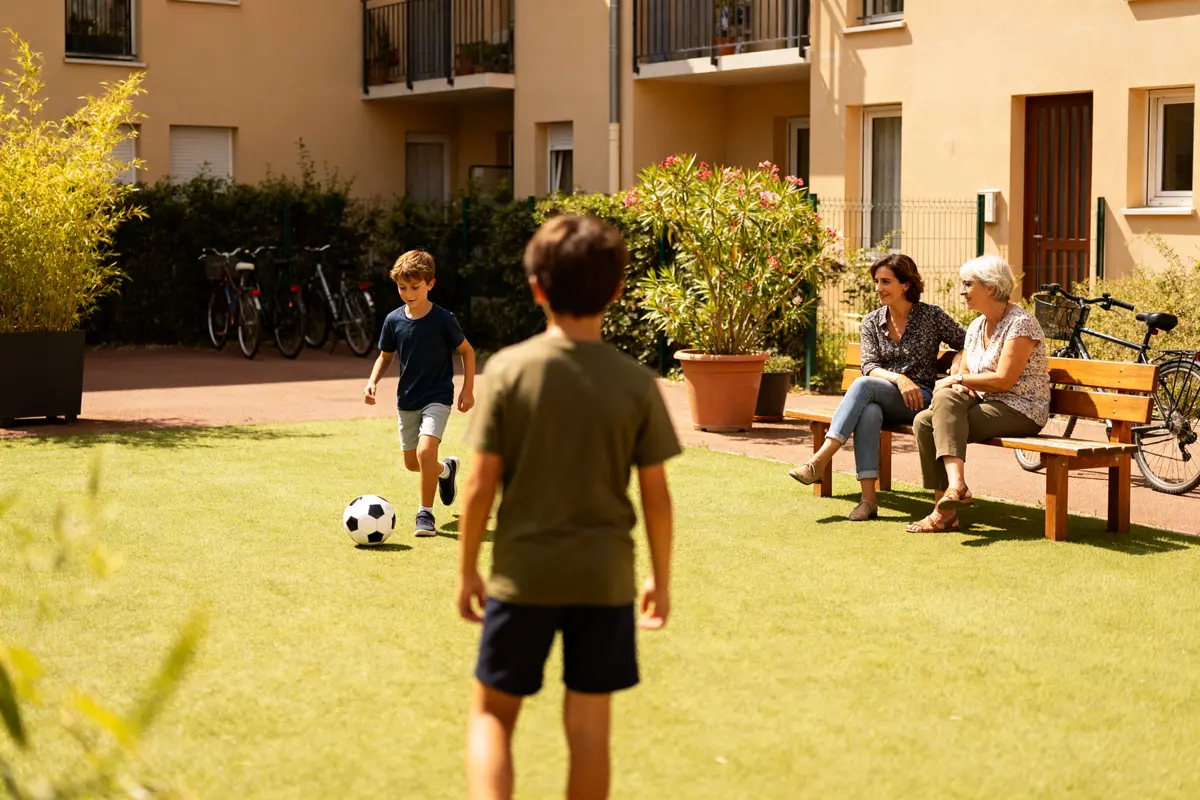 Deux enfants jouent au football dans une résidence de 1001 Vies Habitat avec spectateurs.