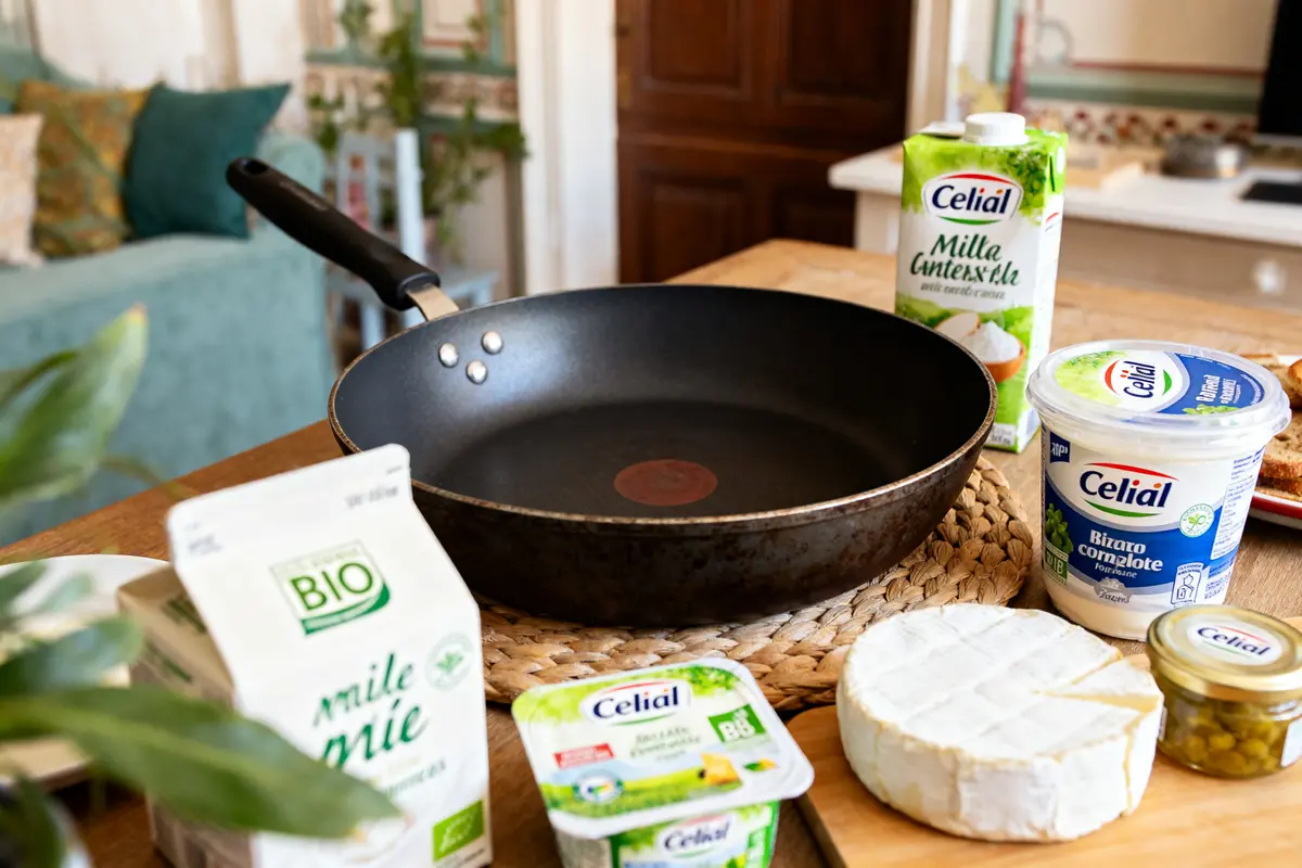 Poêle entourée de produits laitiers et végétaux Celial sur table de cuisine en bois
