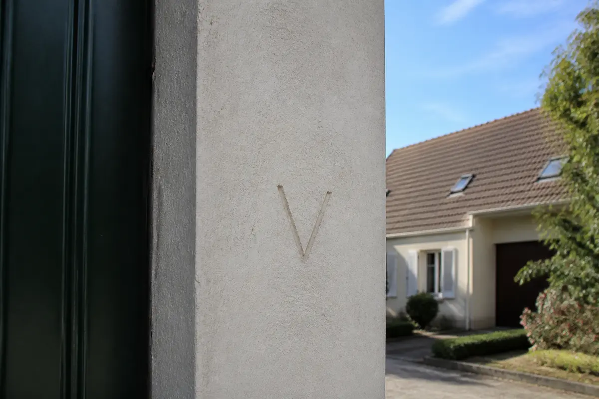 Lettre V gravée sur un mur, signe de cambriolage roumain typique d'avertissement.
